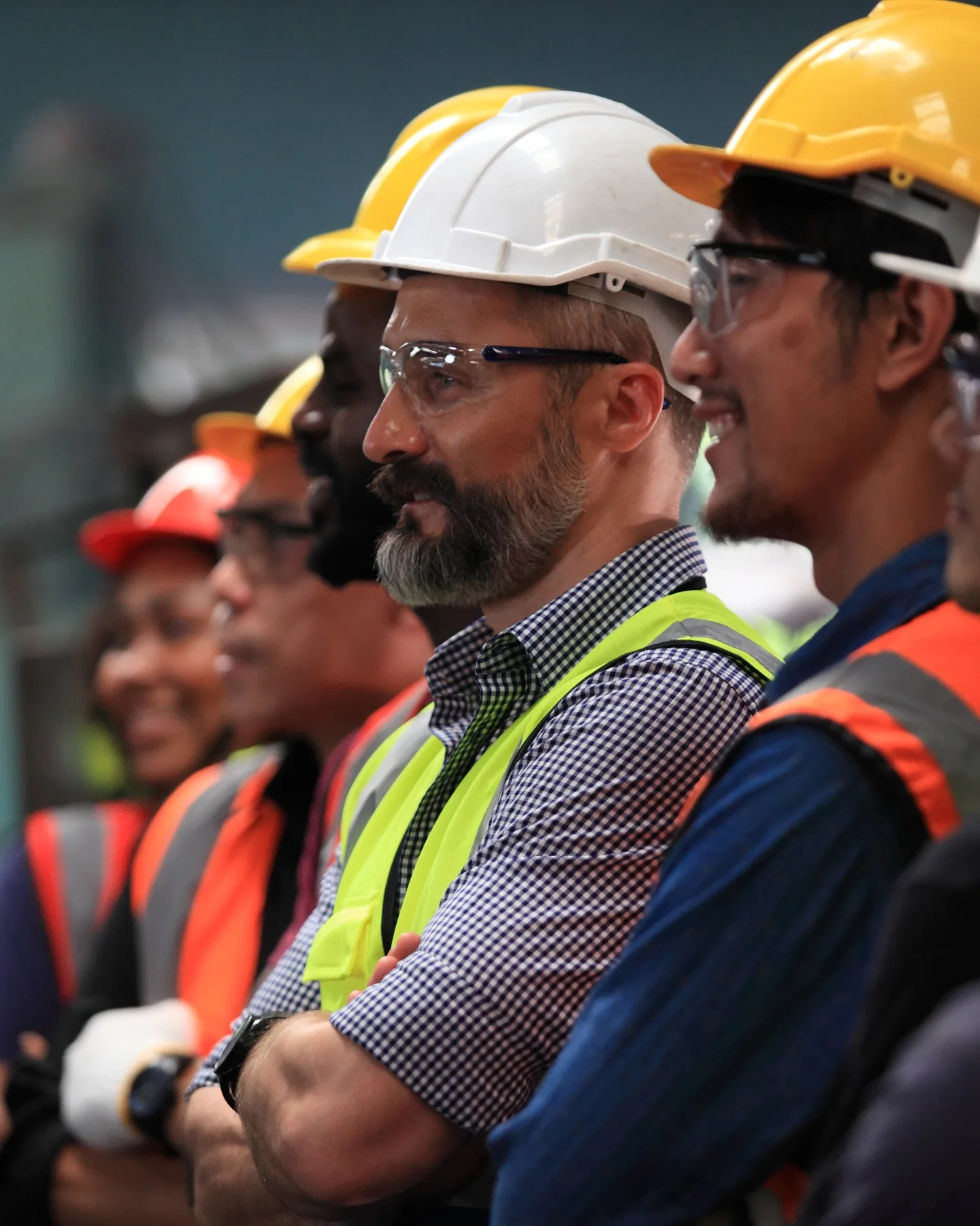 A line of workers in hard hats and high-visibility vests listening at a site briefing.